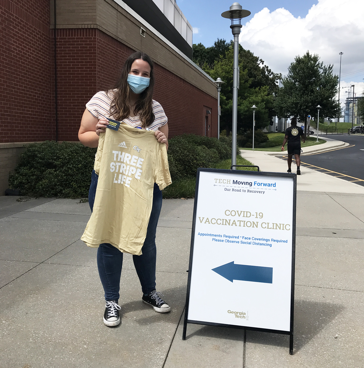 Vaccine clinic volunteer Claire, a third-year student studying biochemistry, holds one of the GT Athletics t-shirts handed out at a recent campus clinic. This month, all students, faculty, and staff who get vaccinated or participate in Covid-19 testing will be eligible for drawings and surprise giveaways of GT Athletics t-shirts and memorabilia, Barnes &amp; Noble at Georgia Tech gift cards, and discount cards for Waffle House, Rusty Taco, and other local businesses.